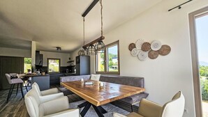 A modern kitchen with a central island, a dining area with a wooden table and chairs, and a large window providing a view of the outdoors.
