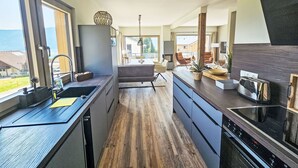 A modern kitchen with a central island, wooden flooring, and large windows offering a view of the outdoors.