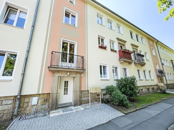 Ein mehrgeschossiges Wohngebäude mit heller Fassade, zahlreichen Fenstern und Balkonen mit Geländern.
