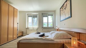 A bedroom with a bed, two windows, a radiator, a wardrobe, a nightstand, and a lamp. - Nice apartment for 4 guests with WIFI, TV and balcony (Dresden)