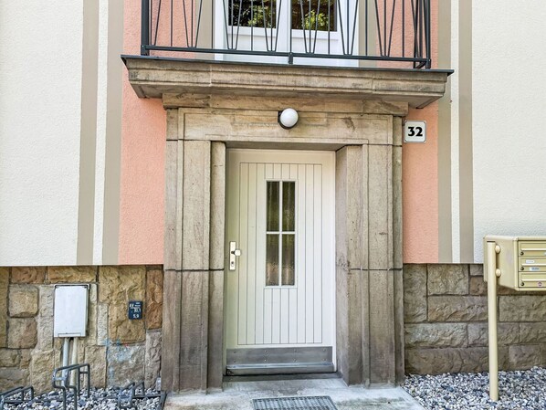 A building entrance with a white door, stone pillars, and a balcony with metal railings.