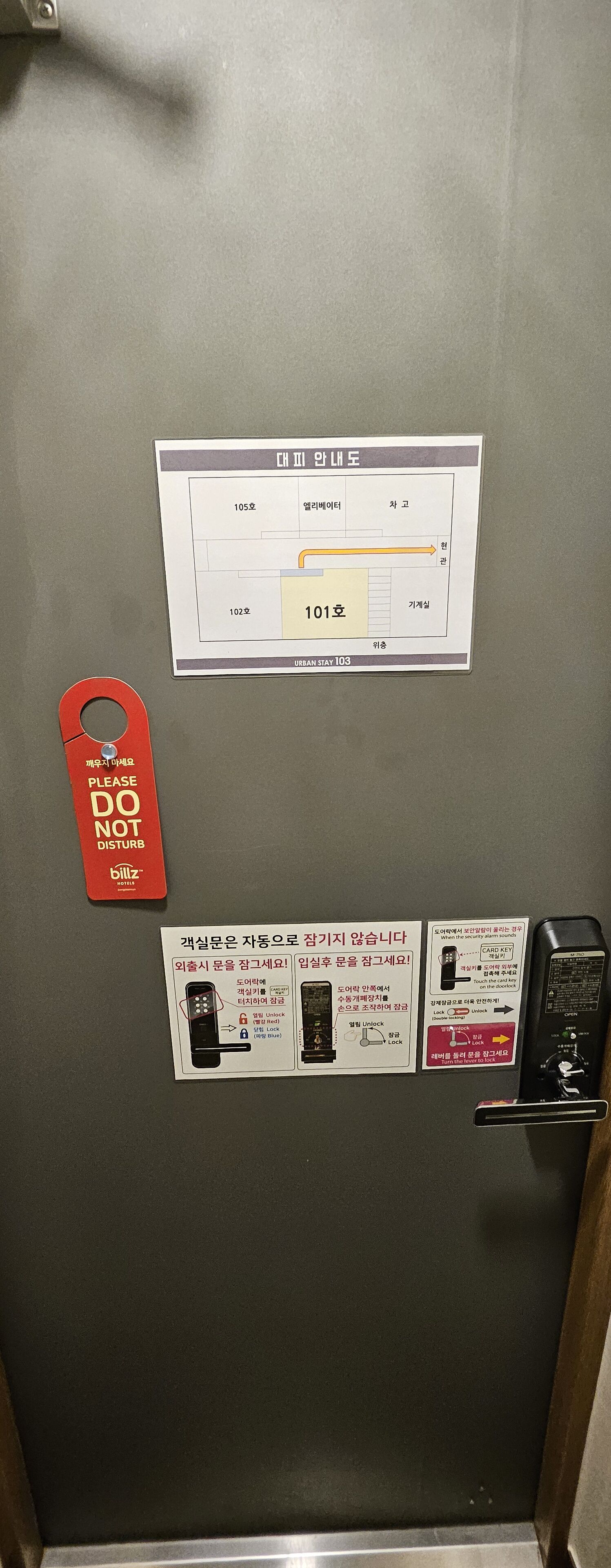 Porta de quarto de hotel com suporte para cartão-chave, placa de número do quarto e painel de instruções de segurança.