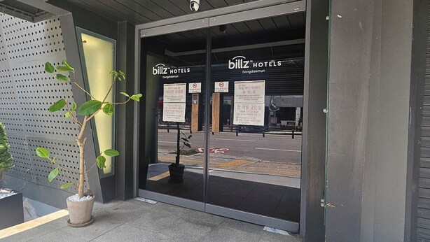The entrance of Billz Hotels with a modern design, featuring a glass door and a potted plant. - Billz Hotel Dongdaemoon  (Seoul)
