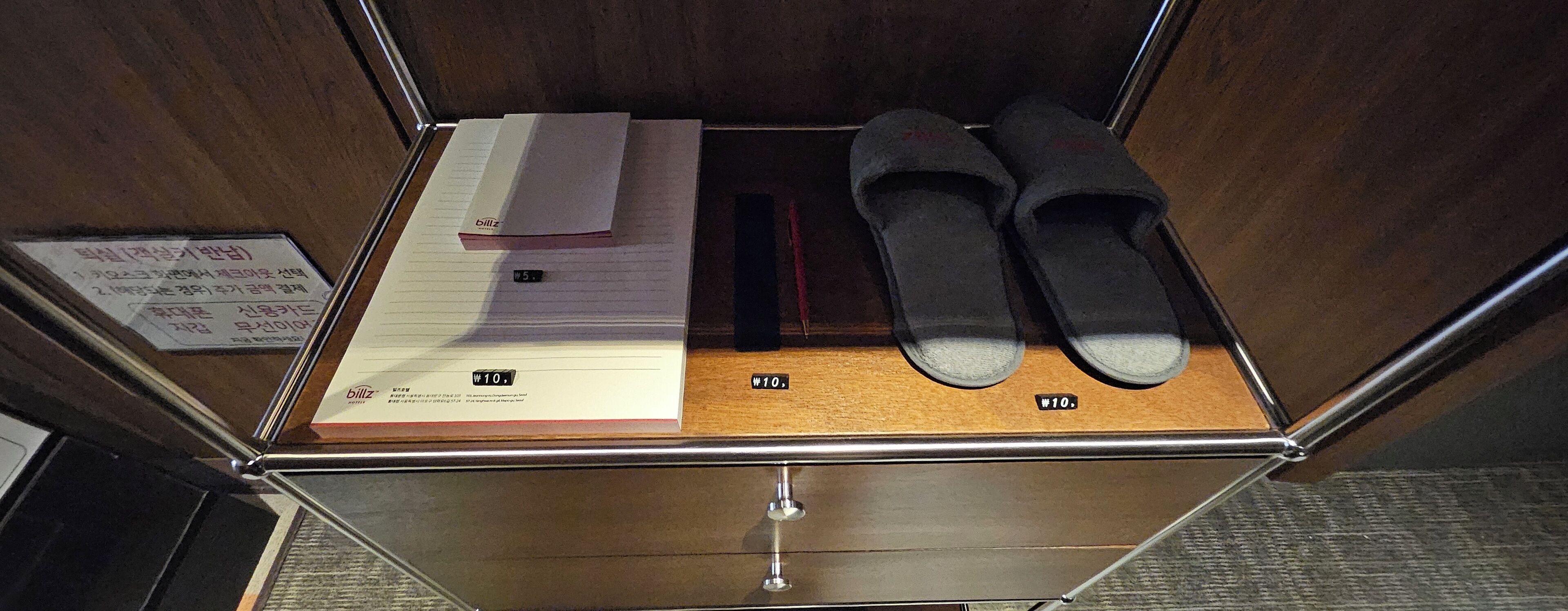 A small wooden compartment with a pair of slippers, a notepad, and a pen.