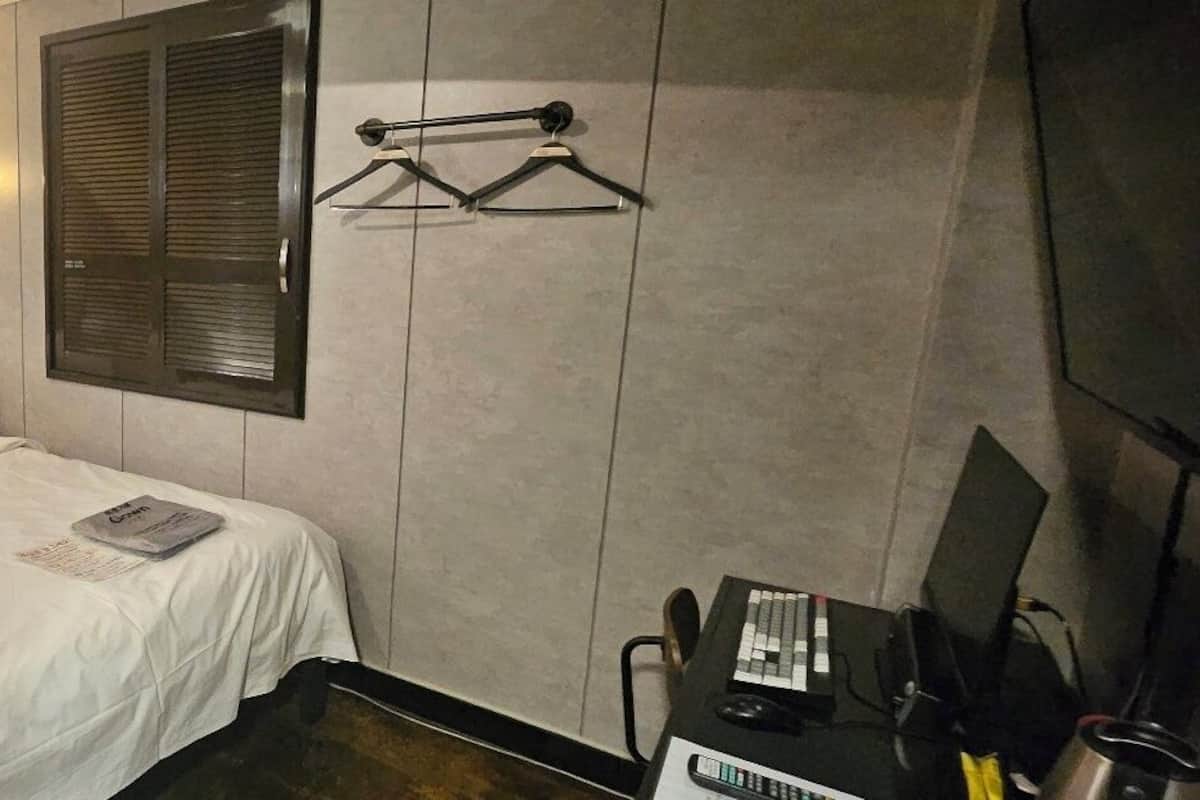 Una habitación de hotel con una cama, un escritorio con teléfono, una lámpara y un televisor instalado en la pared.