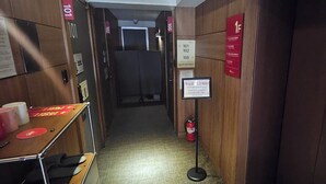 A narrow hallway with wooden walls, numbered signs, a fire extinguisher, and a digital elevator display. - Billz Hotel Dongdaemoon  (Seoul)