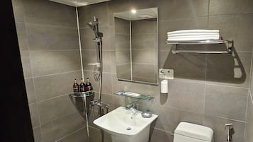 A modern bathroom with a glass shower enclosure, a white sink, and a toilet. There are toiletries on a shelf and a towel rack above the toilet.