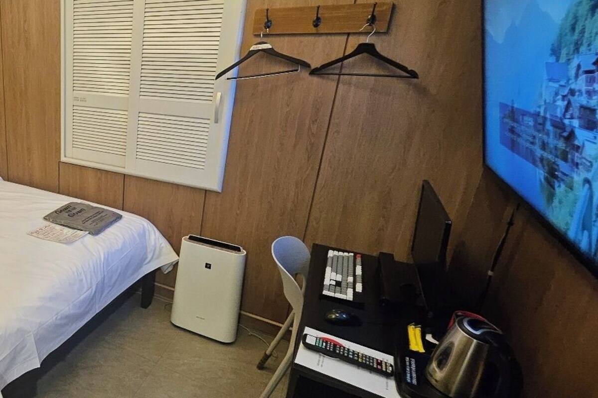 Una habitación de hotel con una cama, un escritorio con computadora, una lámpara, un teléfono y un televisor.