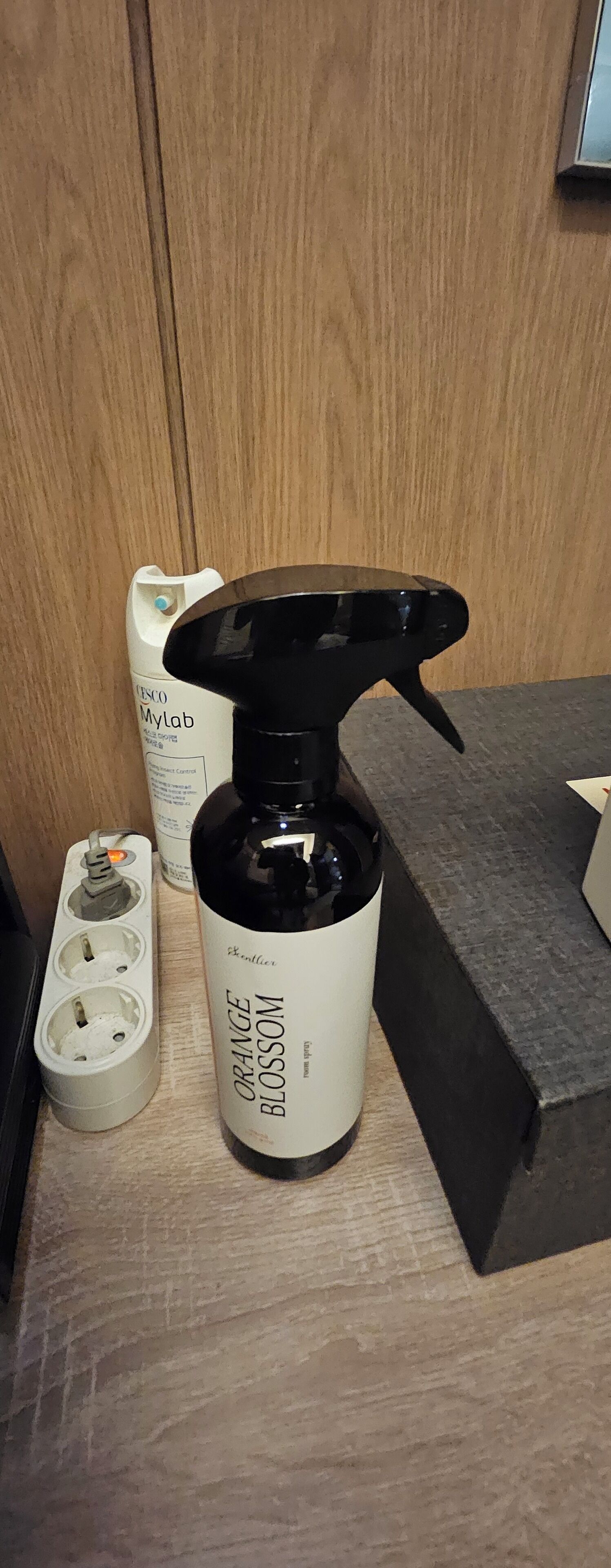 A bathroom with a white sink, a black bottle labeled "Orange Blossom" on the counter, and a white container labeled "Tesco MyLab" in the background.