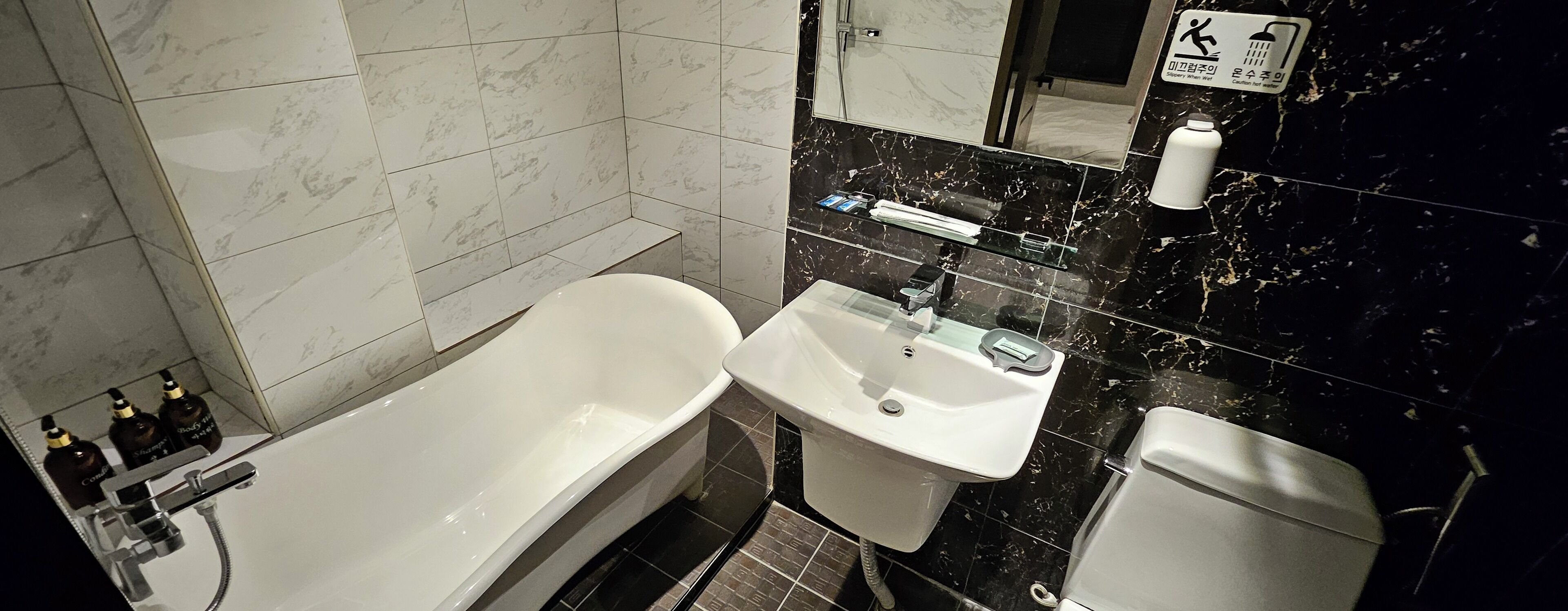 A bathroom with a bathtub, sink, and toilet. There are toiletries on the sink counter.