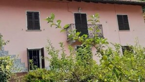 Un edificio rosa con persianas negras, un balcón y una ventana.