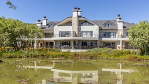 Ein großes, modernes Haus mit zwei Etagen, einem Steinkamin, großen Fenstern und einem Teich im Vordergrund.