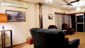 Ett vardagsrum med en takfläkt, en soffa, en fåtölj, en tv och ett fönster med gardiner.