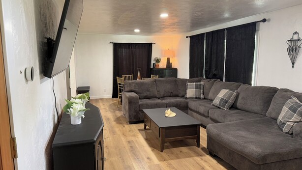A living room with a sectional sofa, a coffee table, a TV mounted on the wall, and a wooden floor. - Farmhouse Fantasy (Nauvoo)