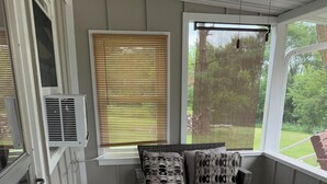 A sunroom with a wicker sofa, patterned rug, and large windows offering a view of the outdoors. - Farmhouse Fantasy (Nauvoo)