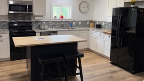 A modern kitchen with white cabinets, a black refrigerator, a microwave, an oven, and a sink. - Farmhouse Fantasy (Nauvoo)