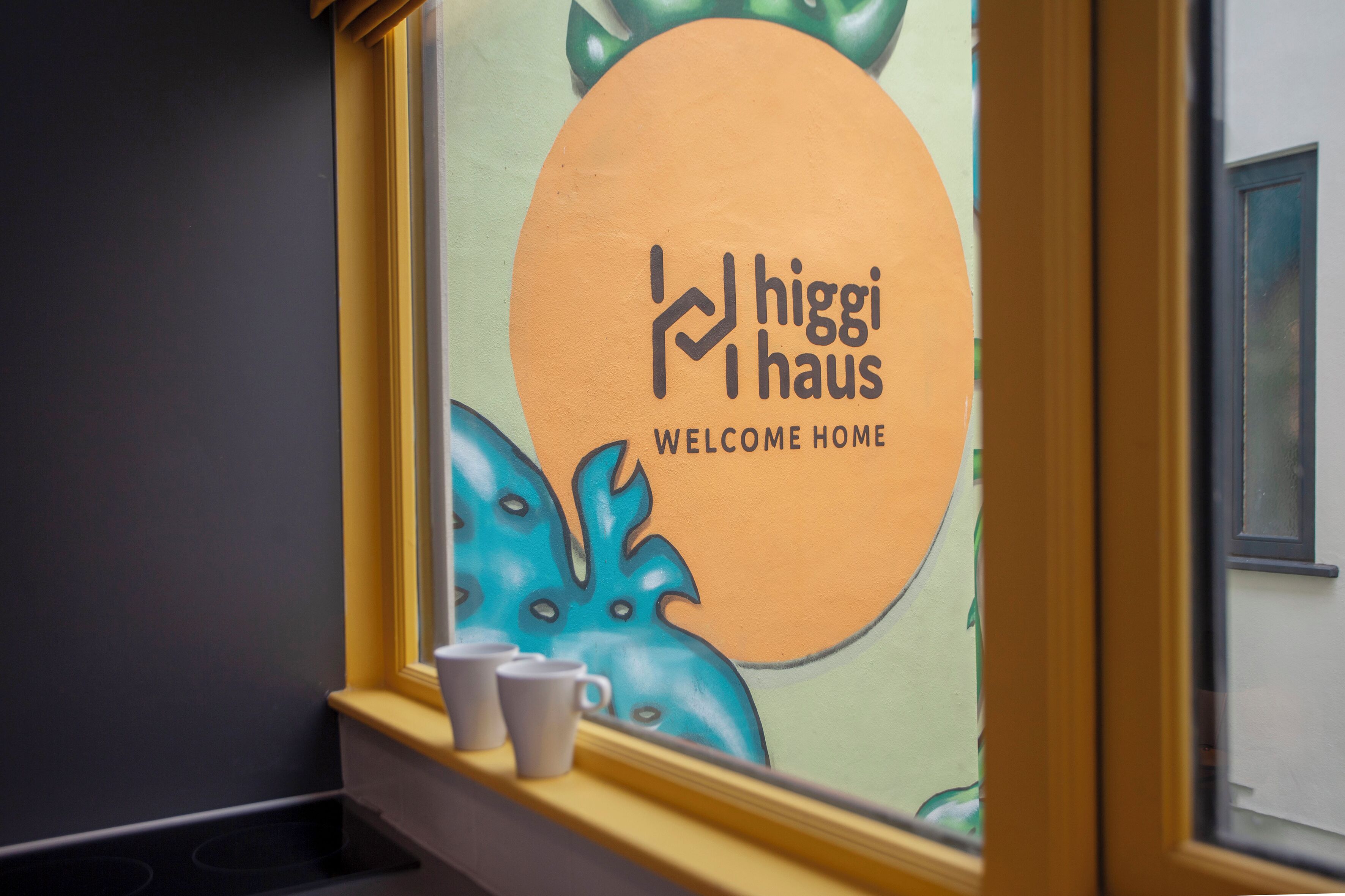 A window with a 'higgi haus' sign and a view of a building's interior.