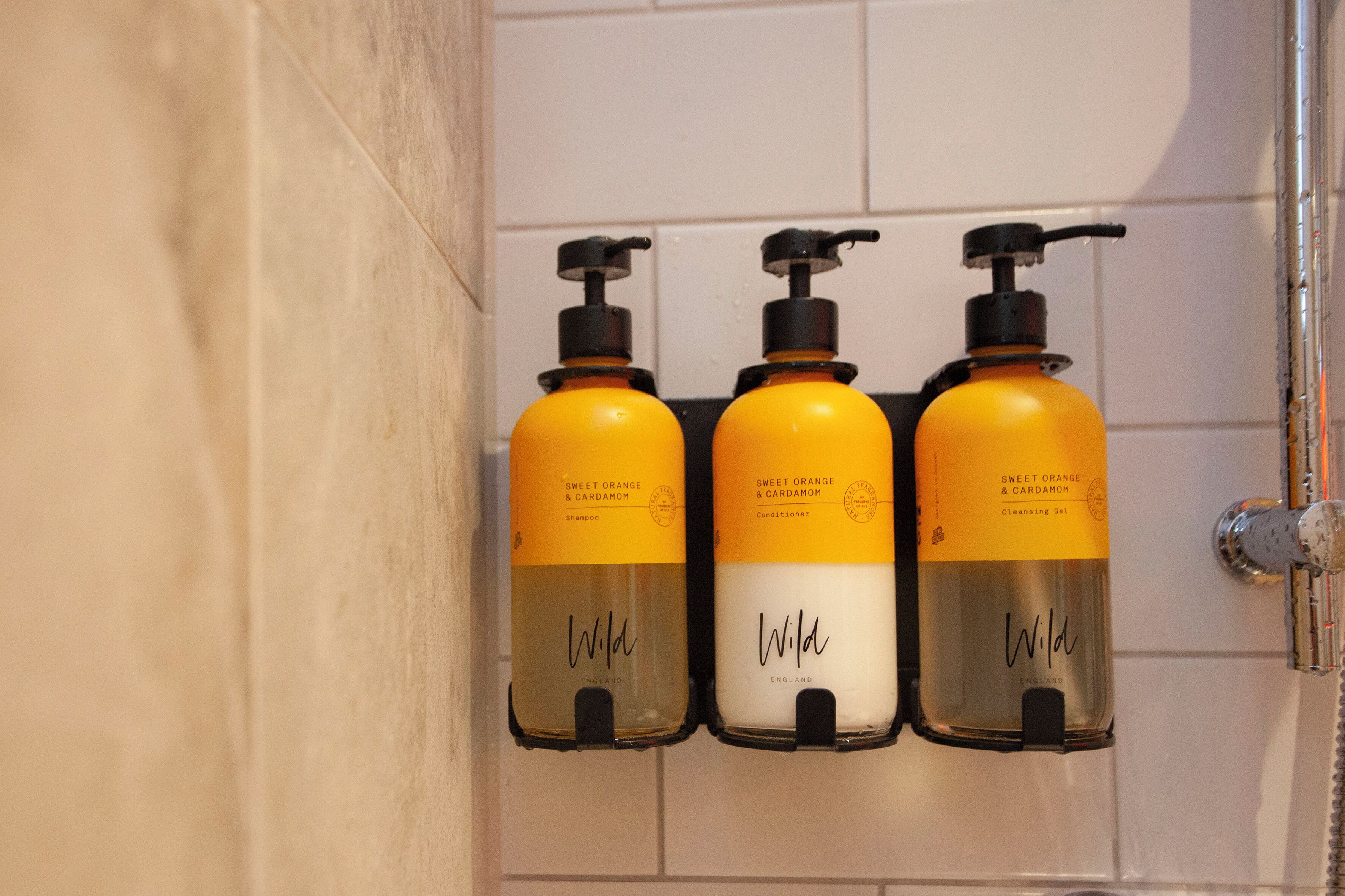 Three bottles of Wild brand toiletries on a wall-mounted dispenser in a bathroom.
