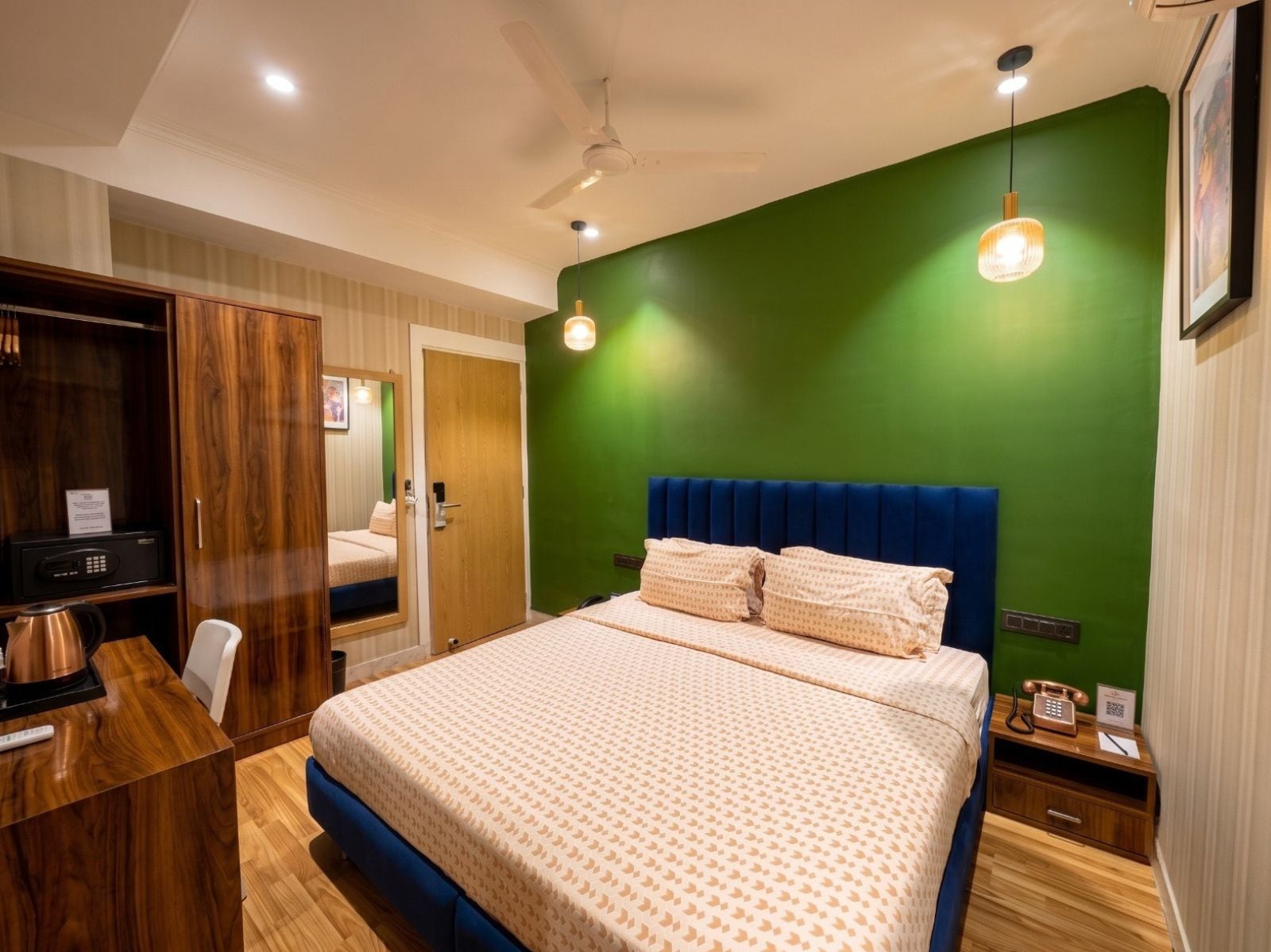 A hotel room with a large bed, a desk, a wardrobe, and a green accent wall.
