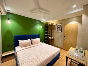 A hotel room with a bed, a desk, a chair, a wardrobe, and a ceiling fan. - asar Connaught Place by Orion Hotels (New Delhi)