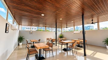 Een eetruimte met houten tafels en stoelen, grote ramen en potplanten.