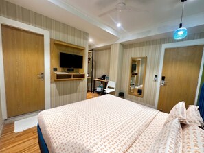 A hotel room with a large bed, a television mounted on the wall, a mirror, and a desk with a chair. - asar Connaught Place by Orion Hotels (New Delhi)