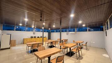 Una habitación amplia con mesas y sillas de madera, una kitchenette y un ventanal con vistas.