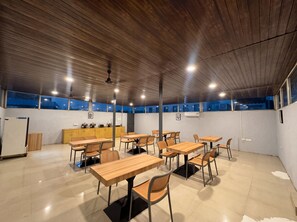 Una habitación amplia con mesas y sillas de madera, una kitchenette y un ventanal con vistas.