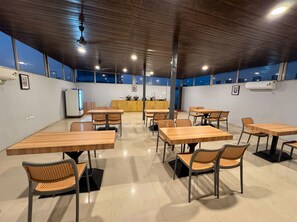 A spacious indoor area with multiple tables and chairs, a kitchen area in the background, and large windows allowing natural light. - asar Connaught Place by Orion Hotels (New Delhi)