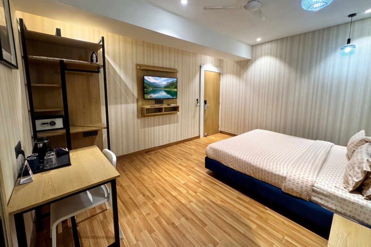 A hotel room with a bed, a desk, a television mounted on the wall, and a ceiling fan.