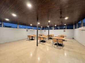 A spacious indoor area with multiple tables and chairs, a high ceiling with wooden beams, and large windows offering a view of the cityscape. - asar Connaught Place by Orion Hotels (New Delhi)
