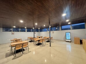 Un espacio interior amplio con varias mesas y sillas, una máquina expendedora y vistas a través de ventanas grandes.