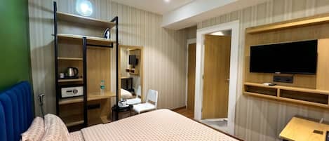 A hotel room with a bed, a desk, a television, a wardrobe, and a mirror.