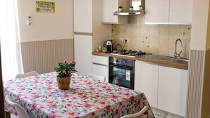 A compact kitchen with white cabinets, a gas stove, and a sink. There's a dining table with chairs and a floral tablecloth.
