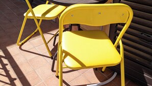 A small outdoor table with two yellow chairs and a potted plant.