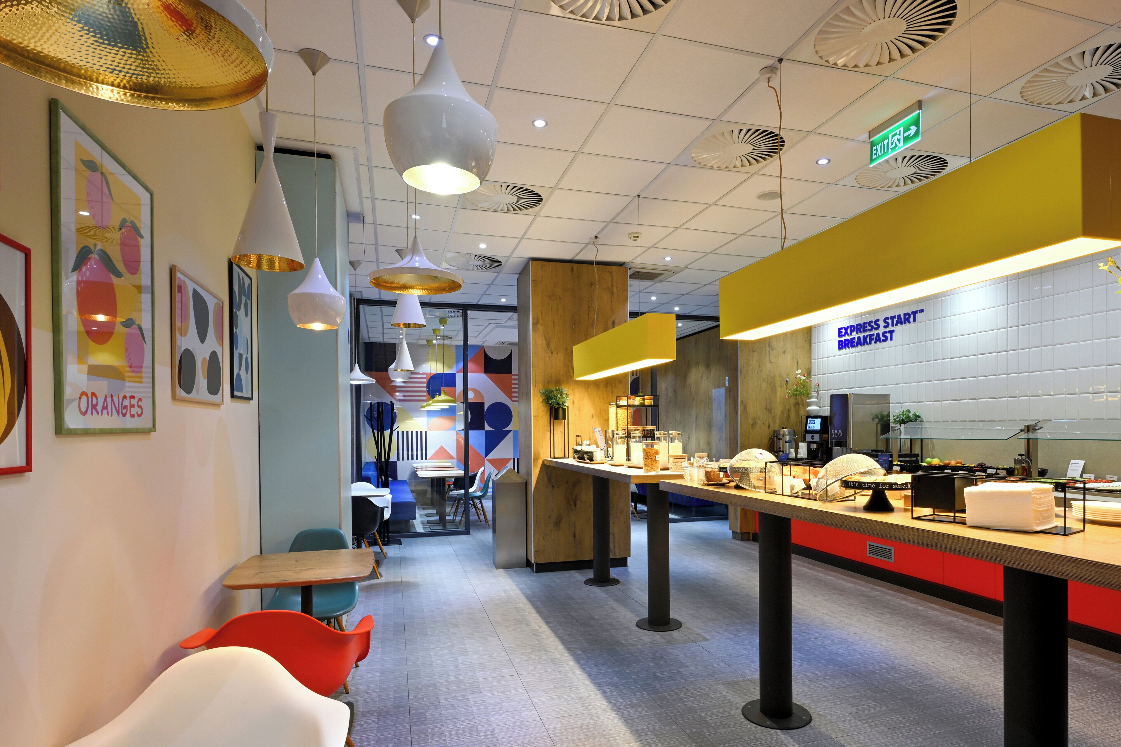 A modern cafe with a breakfast bar, seating area, and a sign indicating an exit.