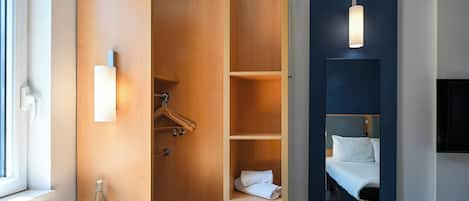 Une chambre d’hôtel avec une armoire en bois, un lit avec une literie blanche, une table de chevet avec une machine à café et un miroir.