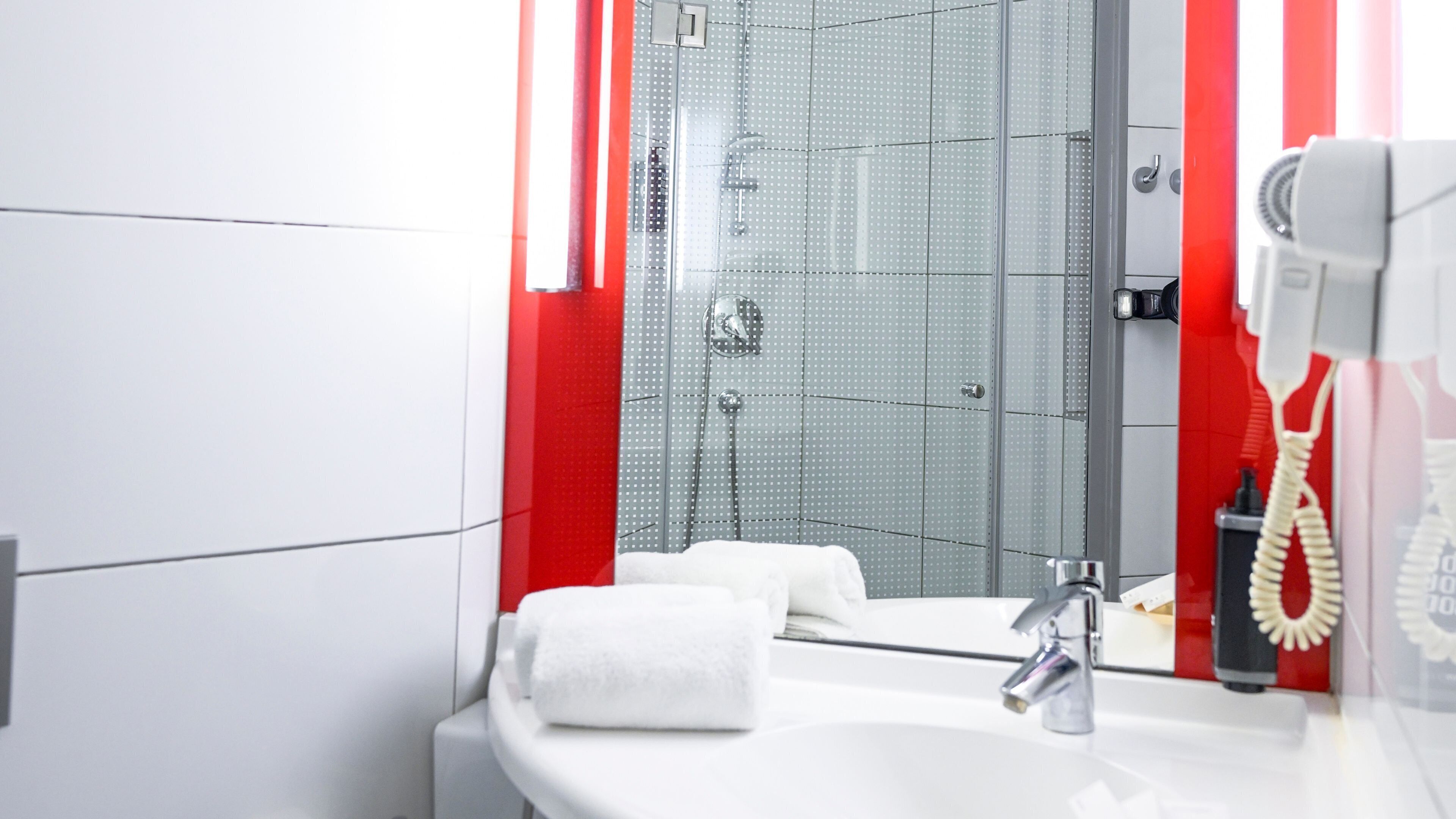 A modern bathroom with a glass shower enclosure, a white sink, and a red-striped shower curtain.