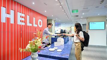 A reception desk with a 'HELLO' sign, a vase with flowers, and a digital screen displaying information.