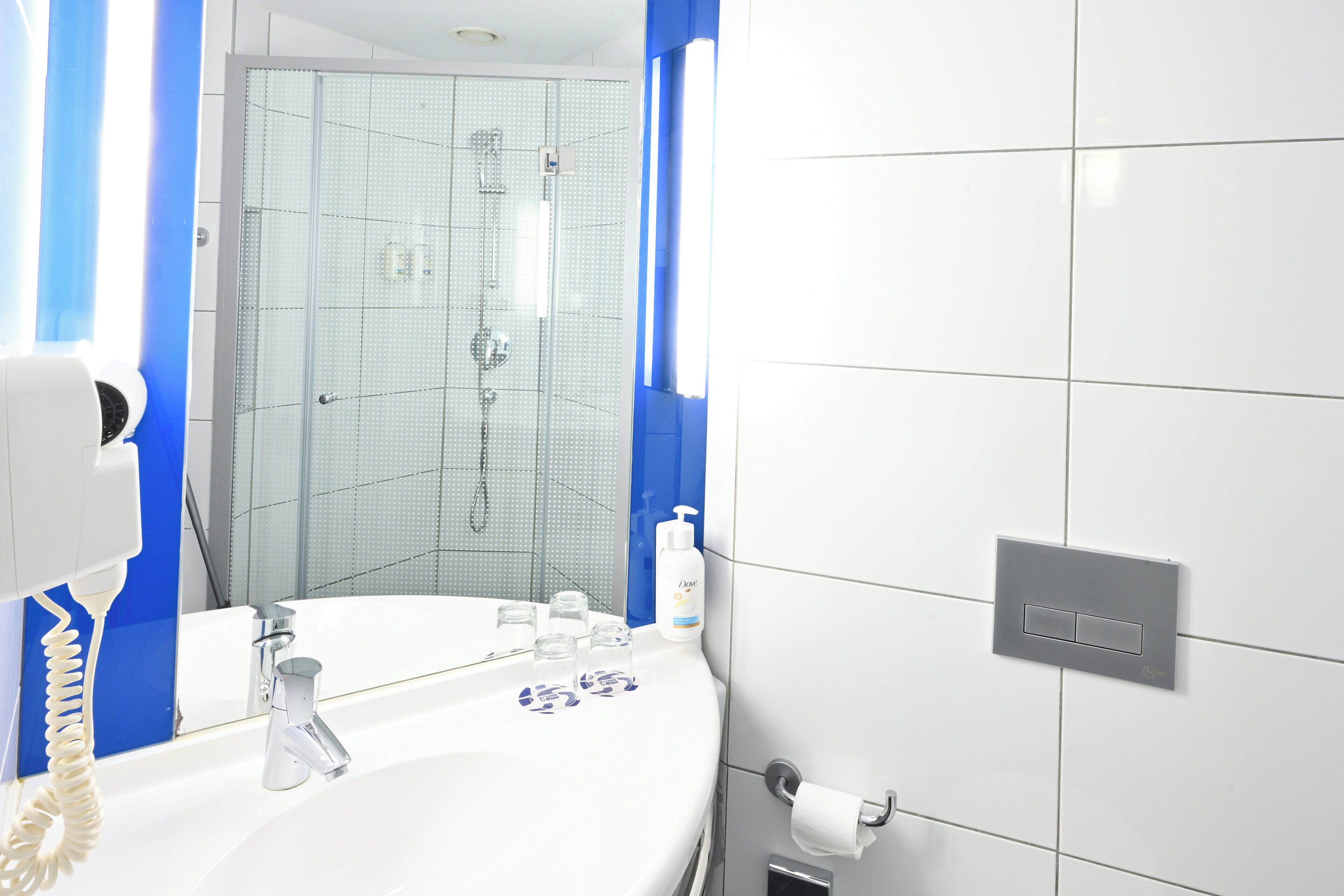 A bathroom with a white sink, a mirror, a shower, and a toilet paper holder.