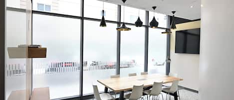 Un salón de conferencias con una mesa grande, sillas, lámparas colgantes y ventanas amplias.