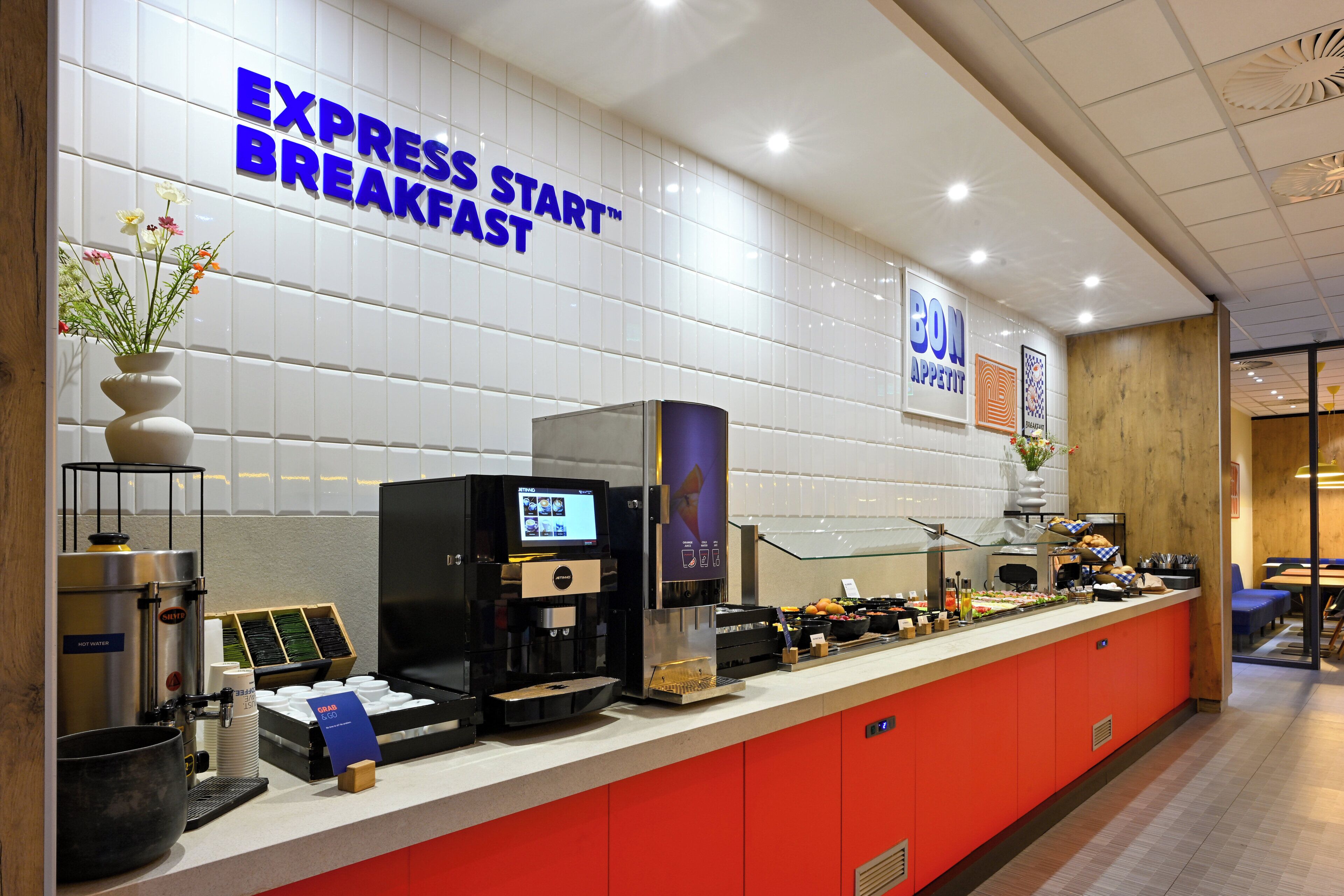 Un comptoir pour prendre le petit-déjeuner, équipé d’une machine à café, d’un écran affichant le menu et d’une pancarte indiquant « PETIT-DÉJEUNER EXPRESS ».