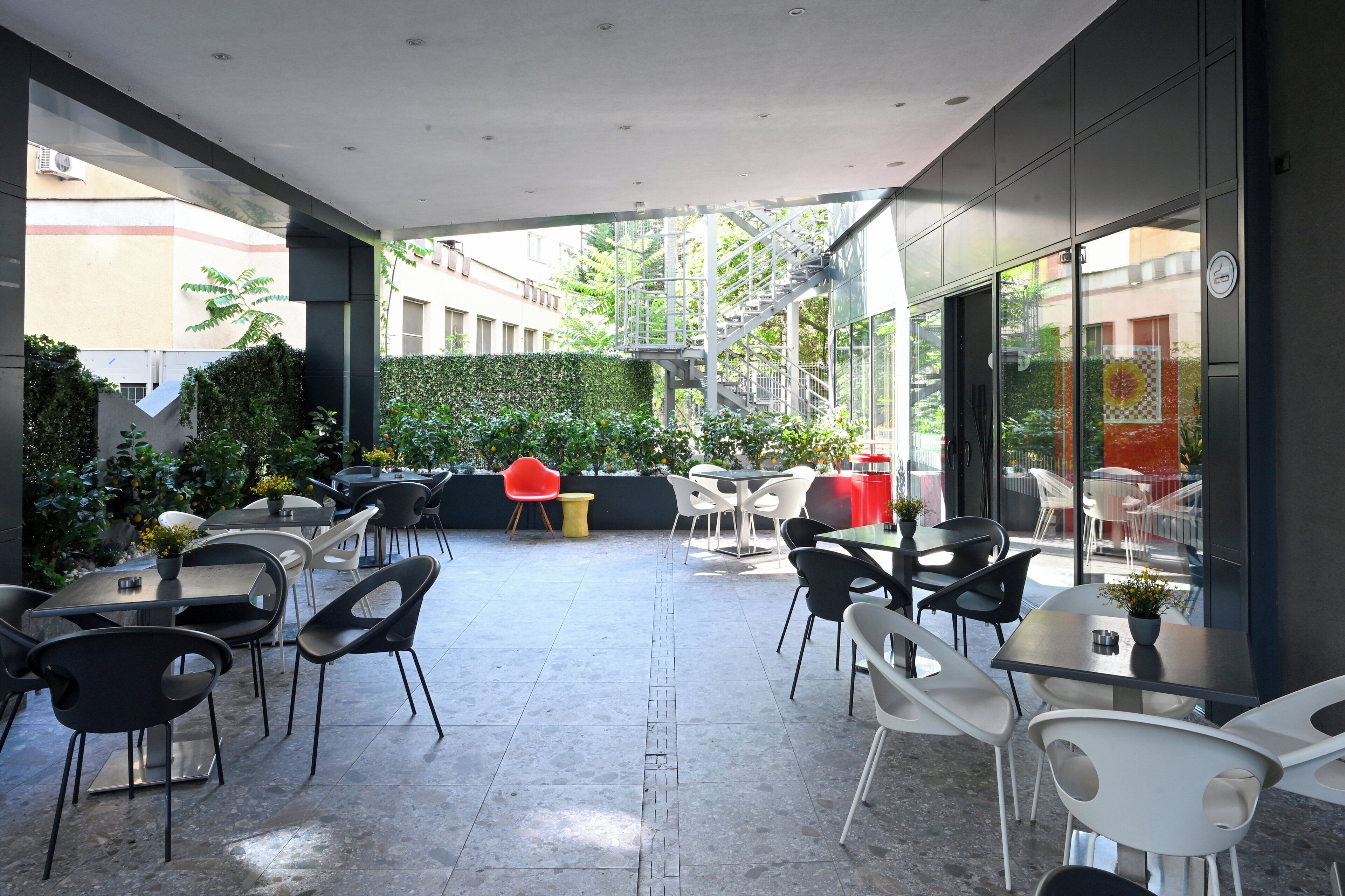 An outdoor patio with tables and chairs, a staircase, and a view of buildings in the background.