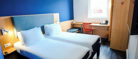 A hotel room with two beds, a desk with a chair, a window, and a door.