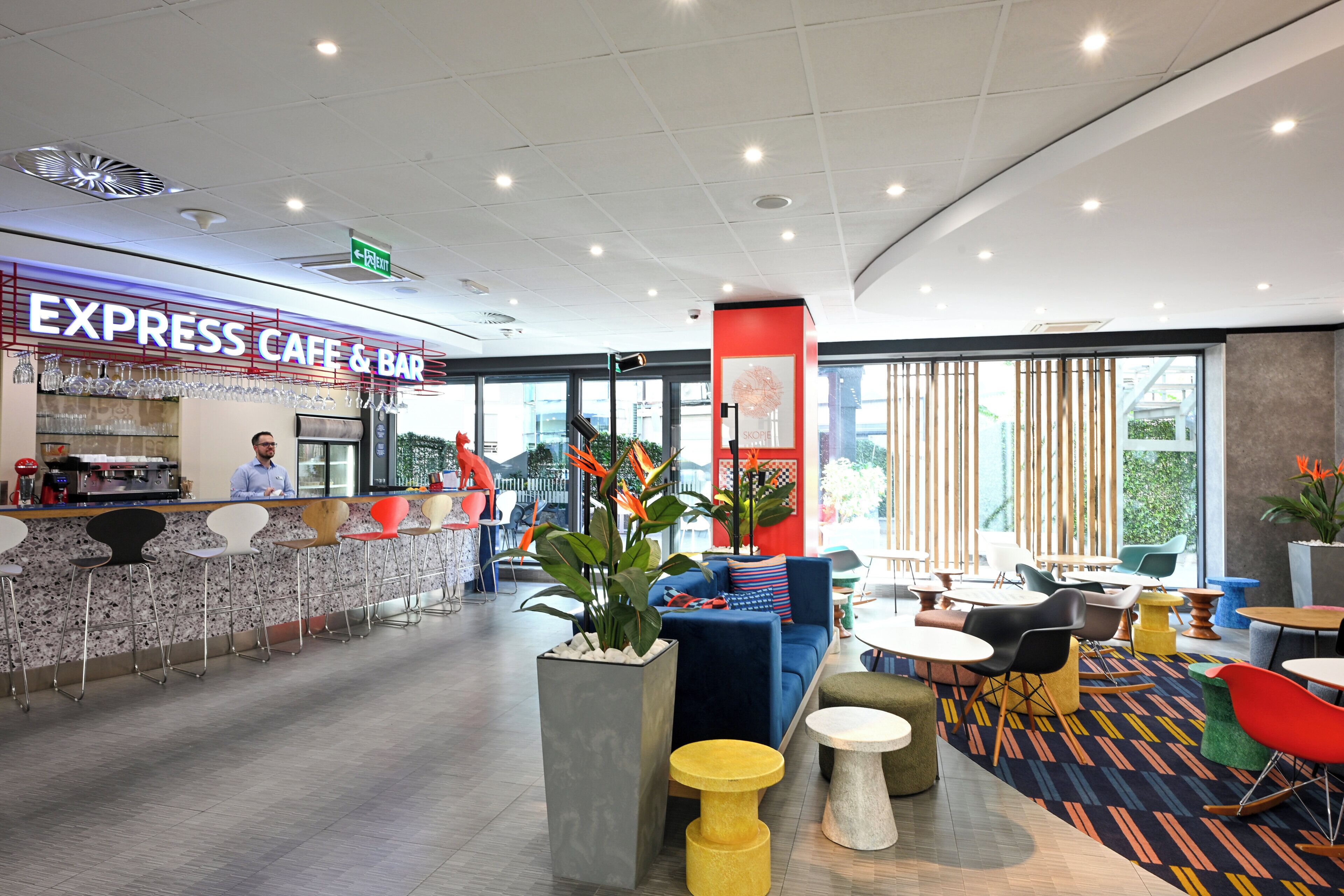 En moderne café med barområde, siddepladser med farverige stole og store vinduer.