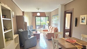 Amplia sala de estar con sofá, sillones, mesa de comedor y área de cocina con armarios y refrigerador.