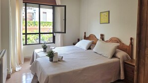 Un dormitorio con una cama grande, una mesita de noche, una lámpara colgante y una ventana con cortinas.