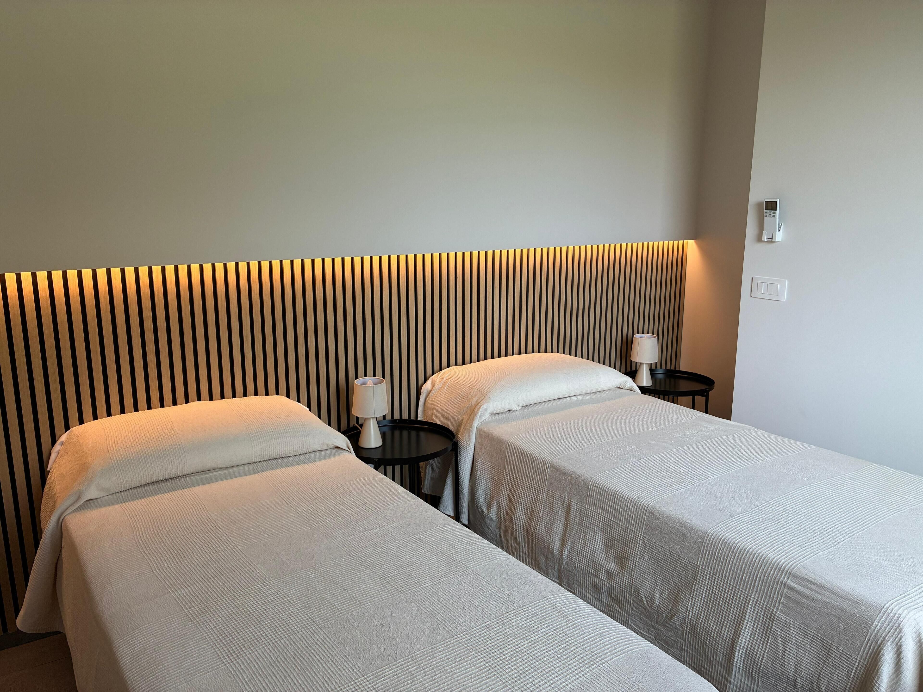 Ein Hotelzimmer mit zwei Betten, einem Nachttisch mit Lampe, Wandleuchte und Steckdose.