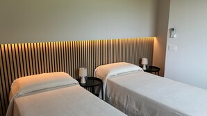 Ein Hotelzimmer mit zwei Betten, einem Nachttisch mit Lampe, Wandleuchte und Steckdose.