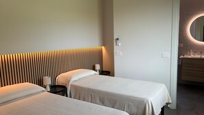 Ein Hotelzimmer mit zwei Betten, einem Nachttisch mit Lampe, einem modernen Kopfteil und einem Badezimmer mit Spiegel und Waschbecken.